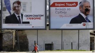 A child rides a toy bike in front of smeared placards featuring populist leader Aleksandar Vucic and former president Boris Tadic in Belgrade, Serbia, on 14 March 2014.