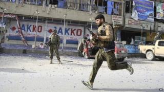 An Afghan army soldier runs into position next to the partly destroyed offices of a TV station