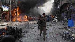 A Pakistani man carrying a child rushes away from the site of a blast shortly after a car exploded in Peshawar, Pakistan, Sunday, Sept. 29, 2013.