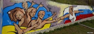 Graffiti depicting Russian President Vladimir Putin (R) extending a hand to the Ukrainian people is seen on a wall in the Crimean city of Simferopol on 28 March 2014.