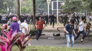 People run as riot police officers (back) try to disperse protesters against a chemical plant project in Maoming, Guangdong province, on 31 March 2014