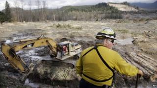 Benton County assistant fire chief Jack Coats surveys the landscape at the scene of a deadly mudslide as an excavator works below to clear a drainage channel, in Oso, Washington 2 April 2014