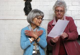 Agnes and another lady are looking at a hymn sheet and signing