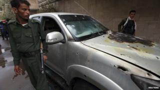 Policemen stand by a damaged car where a French man was assassinated, in Sanaa May 5
