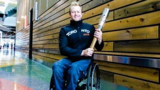 Josh Cassidy, in wheelchair, holds the Queen's Baton.