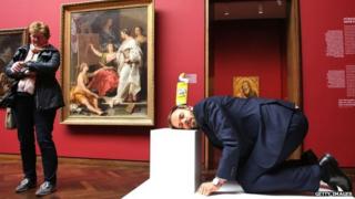 A man crouches with a bottle of toilet cleaner on his head at the Stadel Musuem, Frankfurt