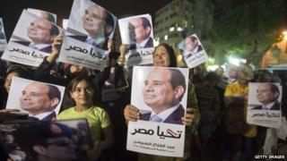 Supporters of Mr Sisi watch a screen in Cairo showing his first television interview