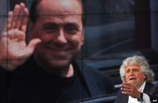 Beppe Grillo speaks on Italian TV with a portrait of Silvio Berlusconi on a giant screen behind him, 19 May