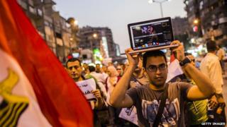 A Egyptian man holding a laptop on his head.