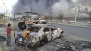 Iraqi children stand next to a vehicle destroyed during clashes between Sunni militants and Iraqi security forces in Mosul (10 June 2014)