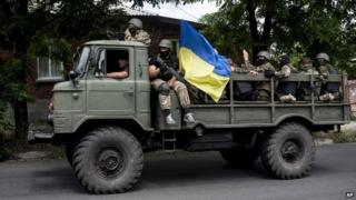 Ukrainian troops with a Ukrainian national flag sit atop a vehicle while they leave a scene of a battle in Mariupol, eastern Ukraine, Friday, June 13, 2014