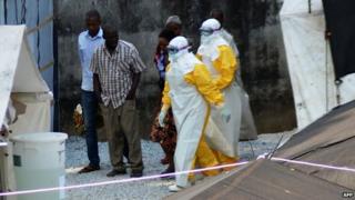 Health workers, wearing protective suits, walking in an isolation centre for people infected with Ebola at Donka Hospital in Conakry on 14 April 2014