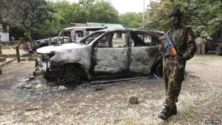 A policeman stands guard near destroyed cars in the coastal Kenyan town of Mpeketoni - 18 June 2014