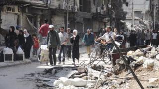 File photo: Residents walk as they receive aid at the Palestinian refugee camp in Yarmouk, south of Damascus 20 May 2014