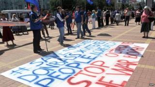 People stand in front of a sign reading "Save Donbass people - Stop the war" at a rally in the eastern Ukrainian city of Lugansk on 29 June 2014