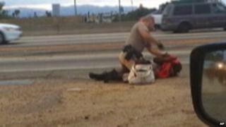 a California Highway Patrol officer straddles a woman while punching her in the head on the shoulder of a Los Angeles freeway 1 July 2014