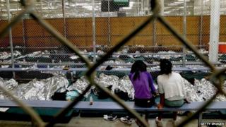 Two young girls watch a World Cup soccer match on a television from their holding area where hundreds of mostly Central American immigrant children are being processed and held at the US Customs and Border Protection Nogales Placement Center in Nogales, Arizona 18 June 2014