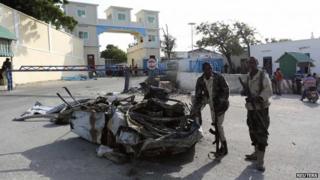 Somali government soldiers stand near the wreckage of a car destroyed during an attack at the presidential palace in the capital Mogadishu July 9, 2014.