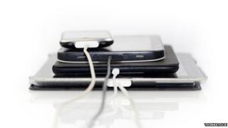 A stack of electronic items with charger wires attached