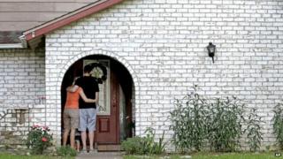 A family who identified themselves as friends of the victims, pauses on the porch after placing flowers and a framed photograph at the door of the home where a gunman killed six people Wednesday in Spring, Texas 10 July 2014