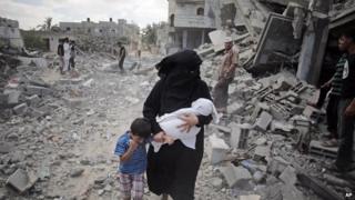 A Palestinian woman passes by rescuers inspecting the rubble of destroyed houses