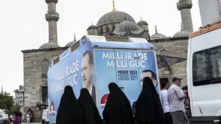 Four Muslim women walk past an election bus supporting Mr Erdogan