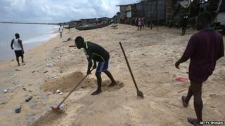 A boy rakes faeces into a hole on the beach in the West Point slum on 19 August 2014 in Monrovia, Liberia