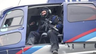A police officer with a high powered weapon scans the ground from a helicopter for a gunman on 1 September 2014, after two people were killed and another injured in Ashburton, New Zealand