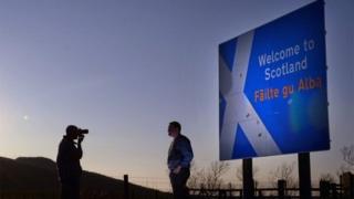 Peoiple take pictures beside a welcome to Scotland sign on the A68 near Carter Bar in Scotland