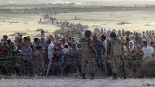 Turkish soldiers stand guard as Syrians wait behind the border fences. 18 Sept 2014
