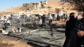 People walk past the charred remains of tents at a refugee camp outside Arsal, Lebanon (25 September 2014)
