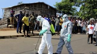 Health workers spray themselves with chlorine disinfectants after removing the body a woman who died of Ebola virus in the Aberdeen district of Freetown, Sierra Leone, on 14 October 2014.