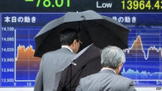 People walk past a share prices board in Tokyo