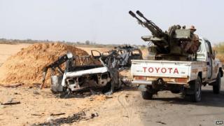 Fighters of Libya"s Fajr Libya (Libyan Dawn) drive their pick up truck mounted with a machine gun near a burnt car, south of the town of Wershfana on October 13, 2014