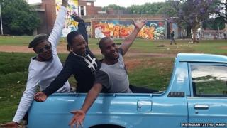 Three people leaning out of a truck with their arms outstretched