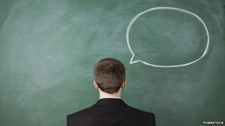 Man with back to camera next to blackboard with speech bubble chalked on