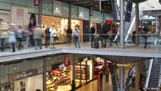 People walk in the shopping gallery of the Gare Saint Lazare railway station in Paris on 30 March 2012