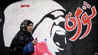 A woman walks past graffiti reading "revolution" in Arabic in December 2011