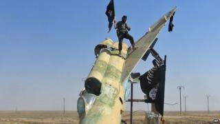 Fighters of the Islamic State wave the group's flag from a damaged display of a government fighter jet following the battle for the Tabqa air base, in Raqqa, Syria
