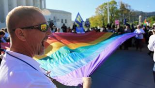 A man holds a giant rainbow flag with several other demonstrators