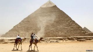Men ride camels in from of the pyramids at Giza