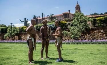 Khoisan Chief SA (C), Khoisan community members Christian Martin (L) and Brendon Willings (R) talk as they camp during the 12th day, outside the South African government "Union Buildings", in Pretoria on December 12, 2017. They were previously refused to enter the buildings by officials who complained about their traditional dress.