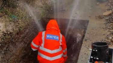 A Severn Trent engineer fixing a burst pipe as water sprays into the air