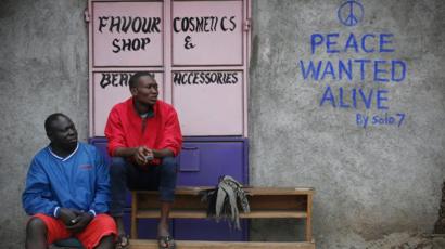 Men sit in front of a wall with a message of peace painted recently by local street artist Solomon Muyundo in Kibera, Nairobi