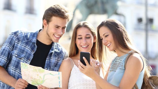 Grupo de 3 jovens com mapa e celular em mãos