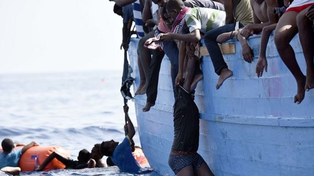 A migrant hangs from a boat as they wait to be rescued as they drift in the Mediterranean Sea, some 12 nautical miles north of Libya, on October 4, 2016.