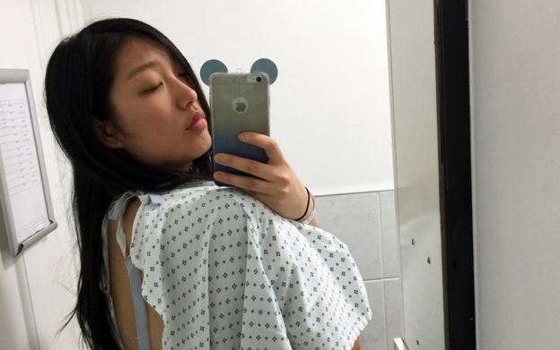 Elaine Chong en bata de hospital tomándose un autorretrato