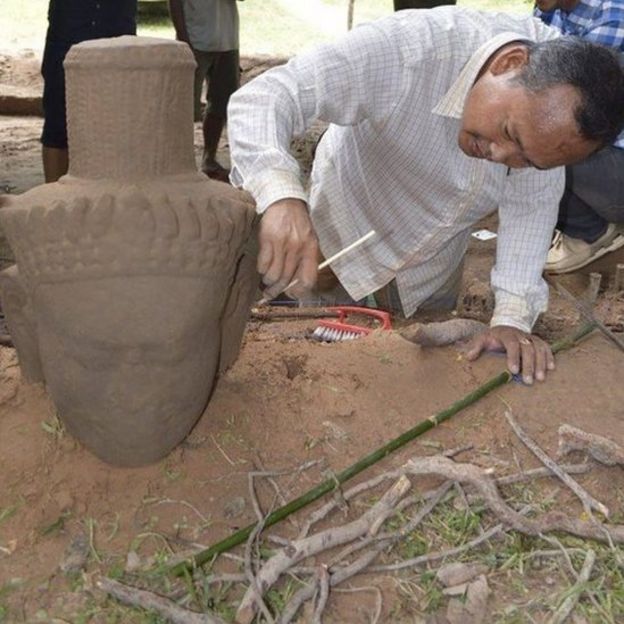 An archaeologist cleans the head of a statue after its excavation from the ground at the complex in Siem Reap province (01 August 2017)