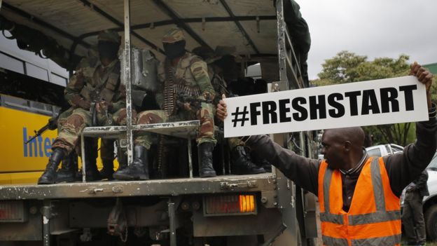 man holding a sign reading #freshstart, next to a vehicle full of soldiers