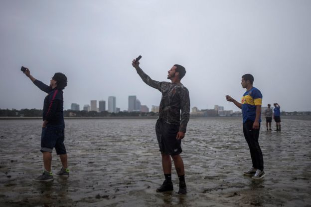 The Tampa skyline is seen in the background as local residents (L-R) Rony Ordonez, Jean Dejesus and Henry Gallego take photographs after walking into Hillsborough Bay ahead of Hurricane Irma in Tampa, Florida, 10 September